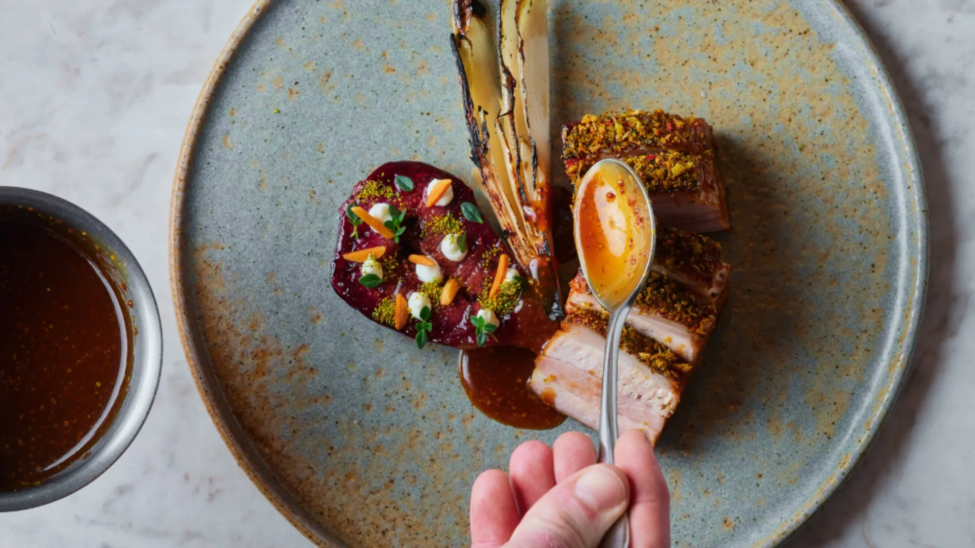 An overhead shot of Omnia's pork belly, drizzled with spoonfuls of sauce. 