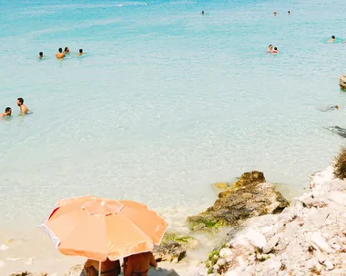 greece, beach umbrella and people swimming in grecian waters