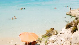 greece, beach umbrella and people swimming in grecian waters