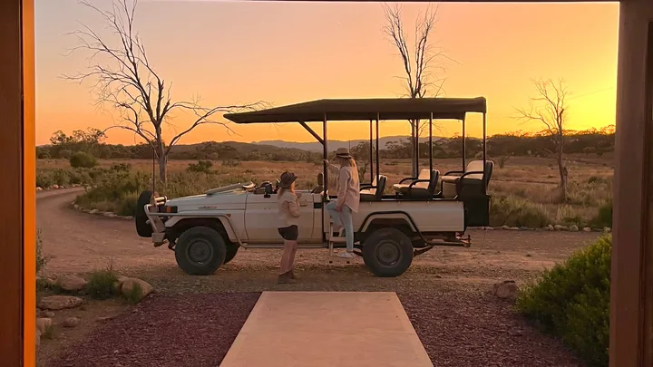 Two people stand talking next to a jeep sitting in front of Arkaba Homestead at sunrise.
