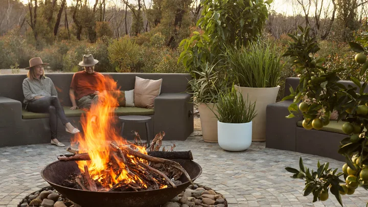 A couple sit in a courtyard with a cosy firepit at the Chalets at Blackheath in the Blue Mountains.
