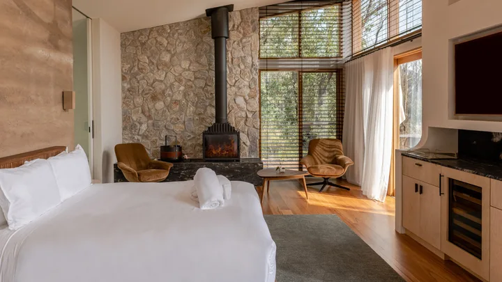 The rustic cosy interior of the bedroom at the Chalets at Blackheath, with a white bedspread and fireplace.