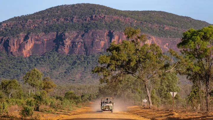A jeep drives up a dirt road in the outback with Mount Mulligan in the background.
