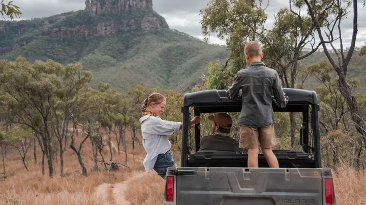 Three people in a jeep driving through the outback.