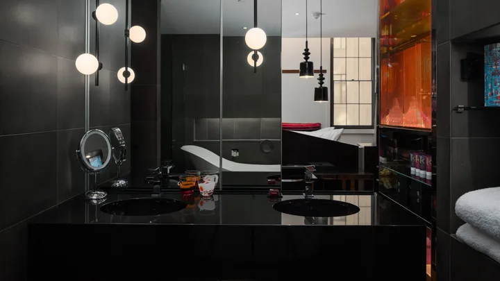 A dark and sleek bathroom at QT Sydney with slipper tub and double recessed sinks.
