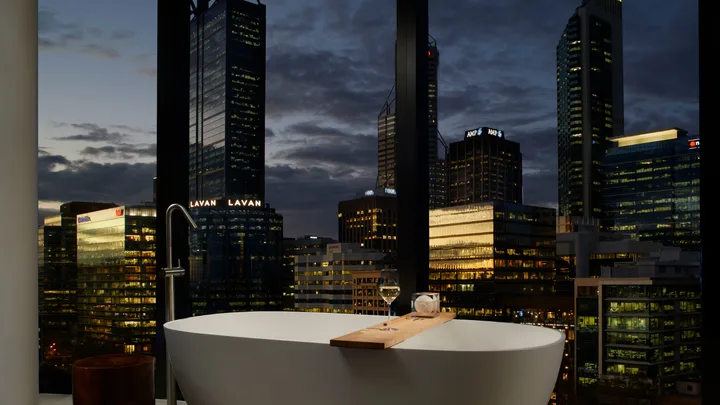 The corner studio bathroom at night overlooking the city at Ritz-Carlton Perth