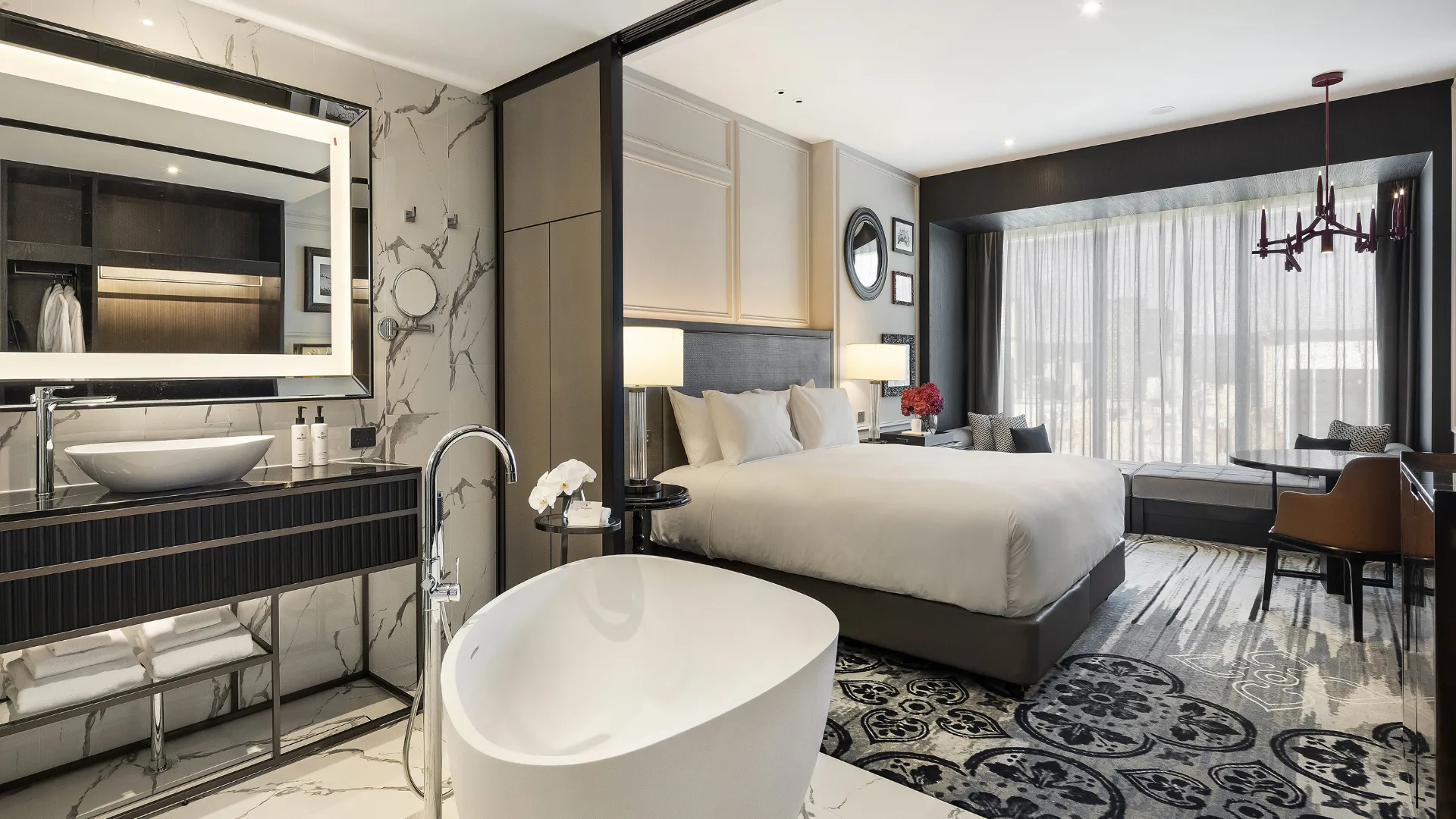The neutral-luxe interior of the Luxury King Suite at the Sofitel Adelaide, with king bed and adjoining bathroom with freestanding bathtub