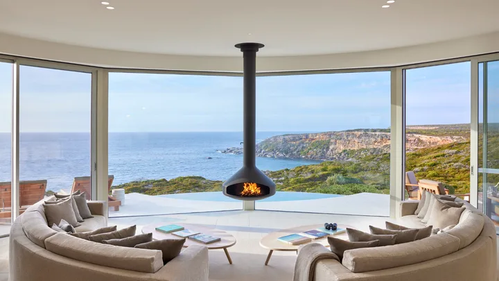 The Pavilion living room at Southern Ocean Lodge has a fire, circular seating and panoramic ocean views