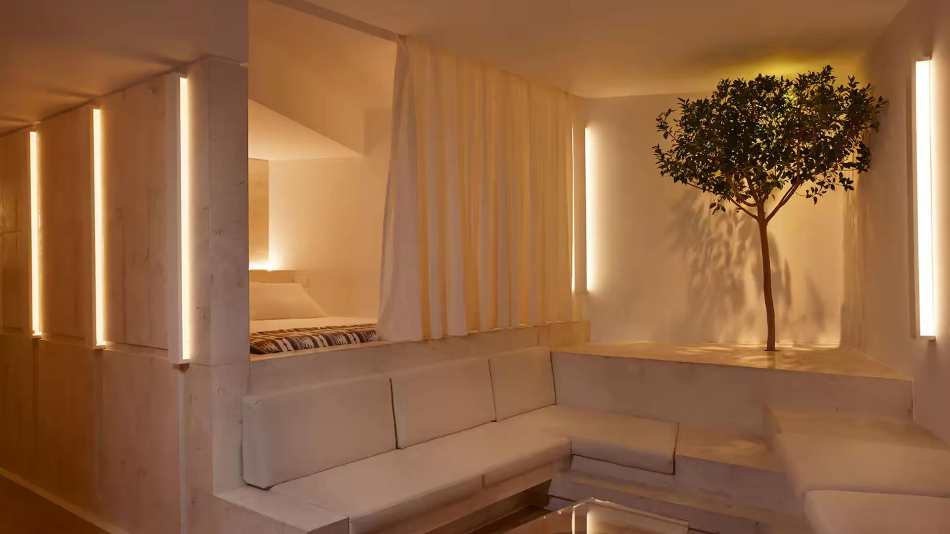 image of apartment in athens with a bed, living space and indoor plant basked in a natural glow