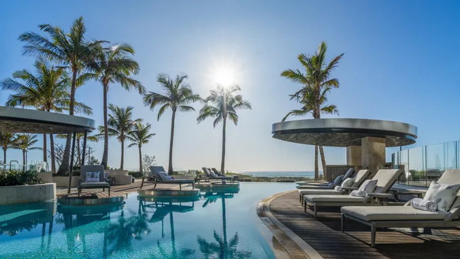 The outdoor pool fringed with palm trees at sunset at Langham Gold Coast.