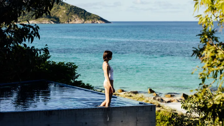 A woman stands at the edge of an infinity pool overlooking the ocean at Lizard Island, Queensland.