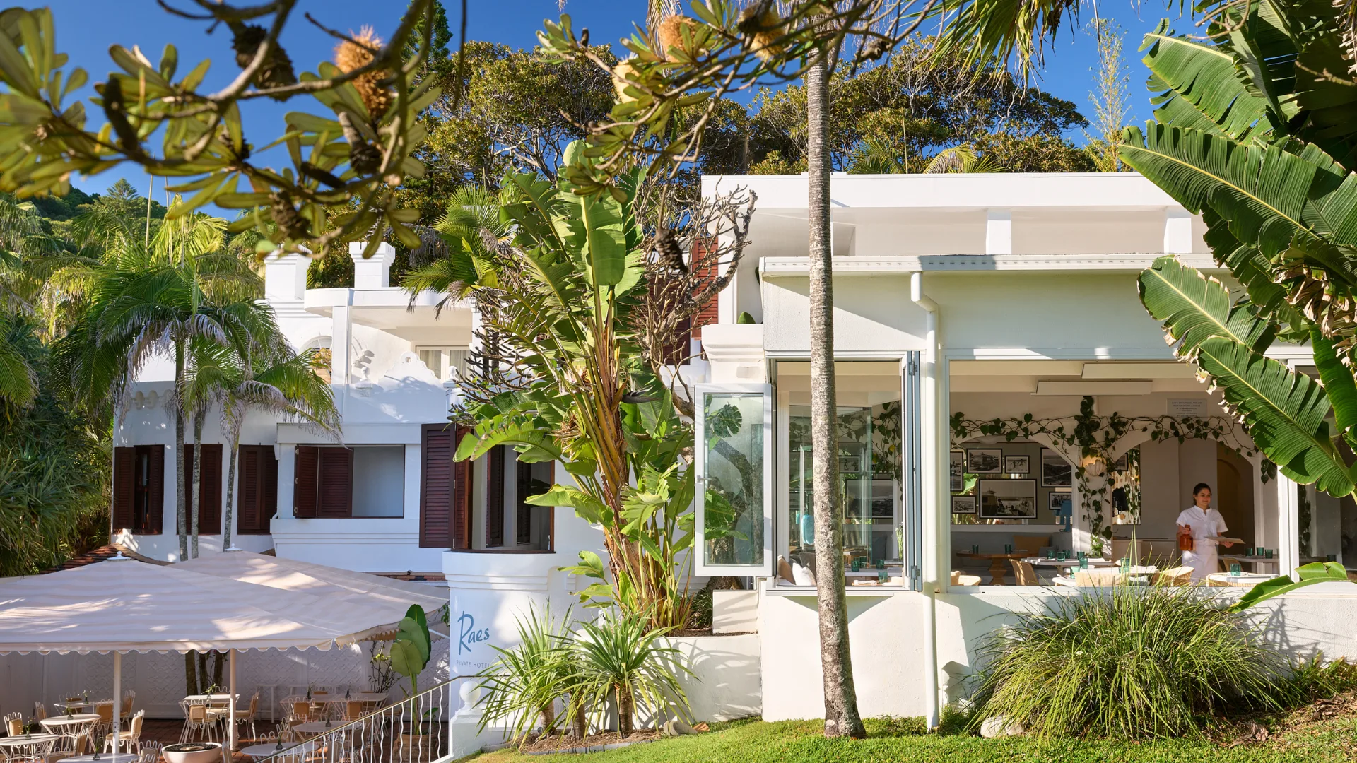 The dreamy white-washed exterior of Raes on Watego, surrounded by palm trees and lush gardens at Raes on Wategos.