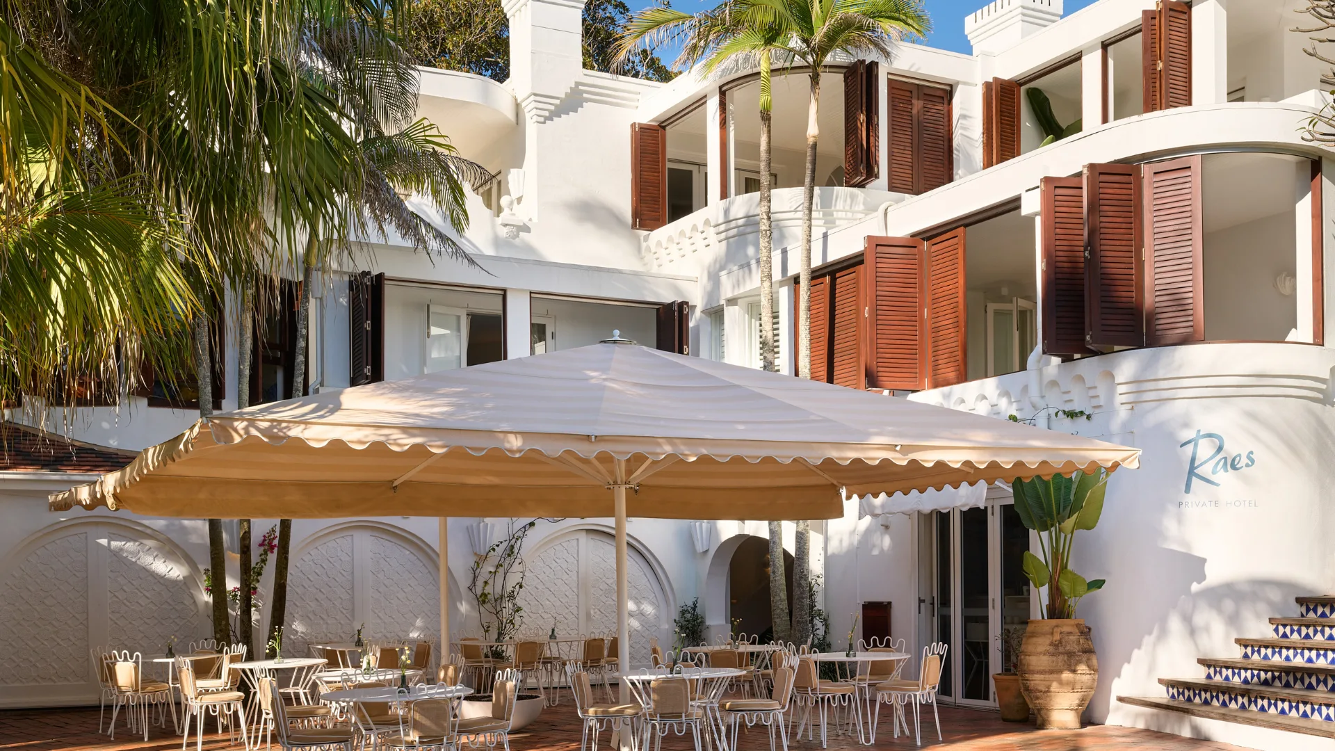 A casual terraced dining area with white umbrellas outside Raes on Wategos.