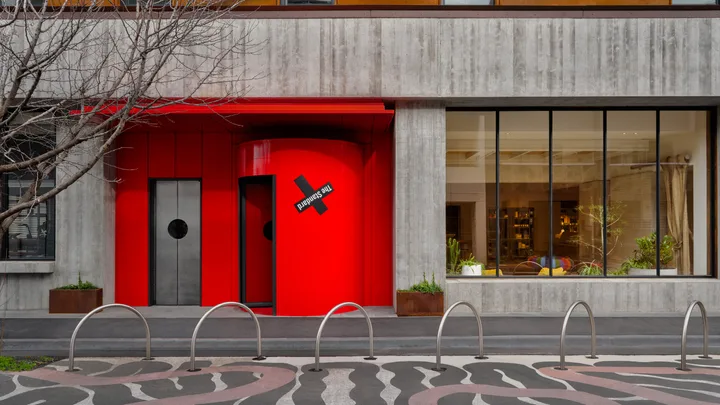 The cool grey exterior of the StandardX Melbourne with a bright red door and entryway
