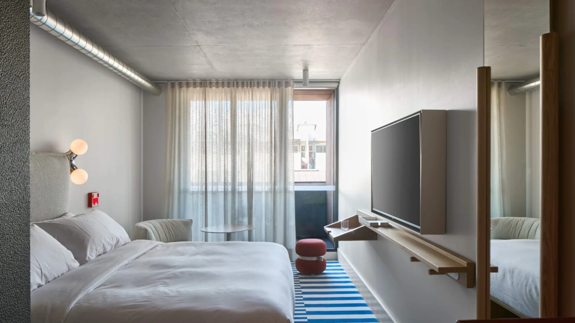 The King Urban View suite at StandardX Melbourne with crisp white bedlinen and blue striped rug.