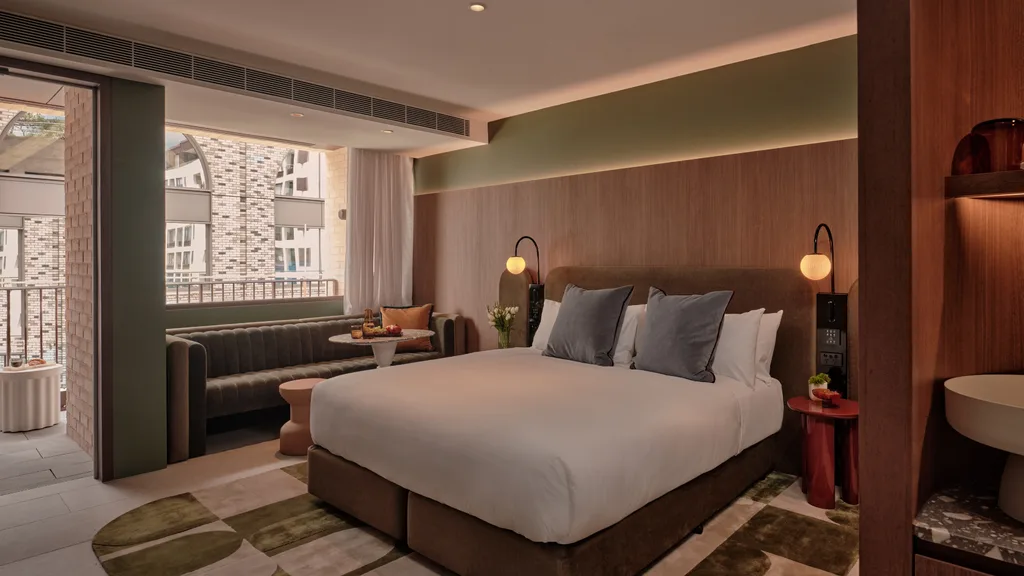Timber and olive tones in the bedroom suite, with sofa and private balcony at The Eve Hotel, Sydney