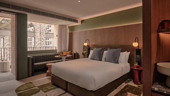 Timber and olive tones in the bedroom suite, with sofa and private balcony at The Eve Hotel, Sydney