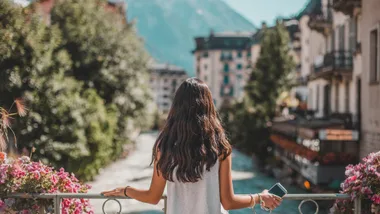 A woman looking at the mountains in France, phone in hand. The best eSIM for international travel will keep you connected without paying a premium in Europe and beyond.