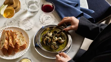 Loulou escargot soaked in herbed oil with a plate of bread and wine on the side