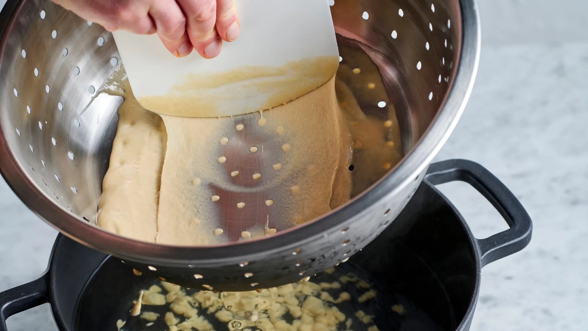 Pushing dough batter through a metal colander 