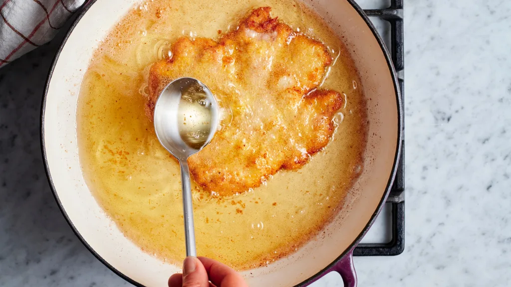 Golden battered schnitzel being shallow-fried in a pan