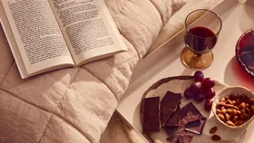 A cosy spread of wine, chocolate and almonds with an open book.