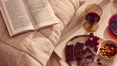 A cosy spread of wine, chocolate and almonds with an open book.