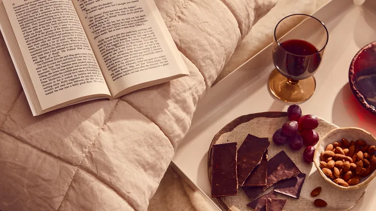 A cosy spread of wine, chocolate and almonds with an open book.