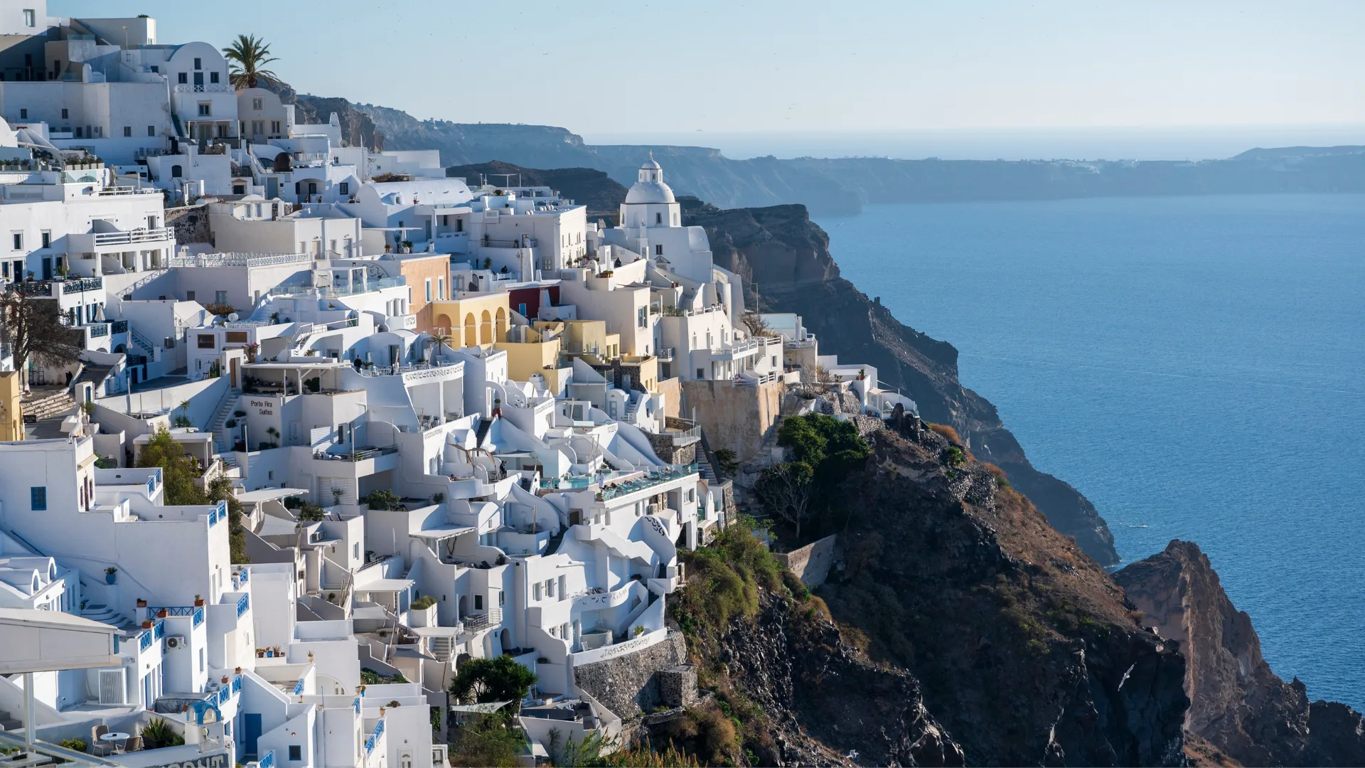 A great view overlooking the town of Fira in Santorini. Taken late afternoon when the light is gently bathing the buildings of the town. You can see the sea of The Caldera in the distance below the rocky steep hillside the town is built on.