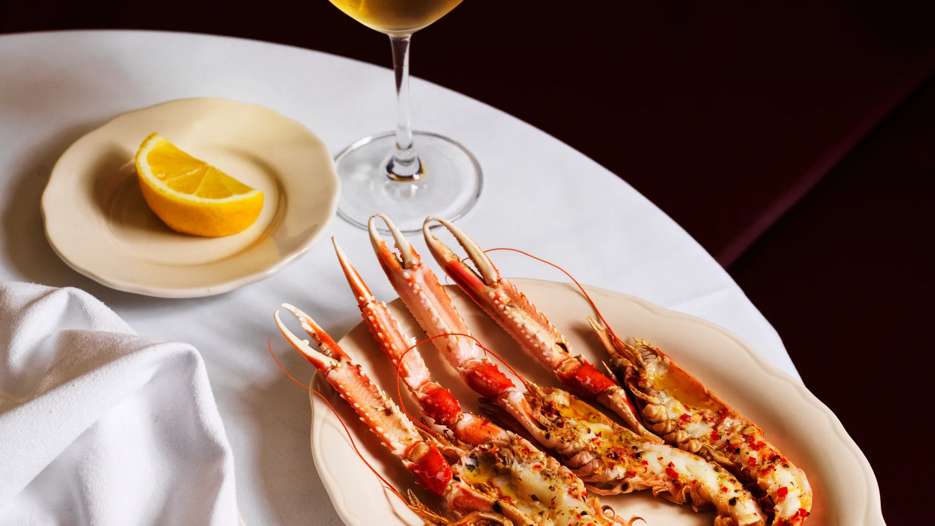 A plate of grilled scampi on a table at Sydney restaurant Vin-Cenzo's with a slice of lemon and white wine