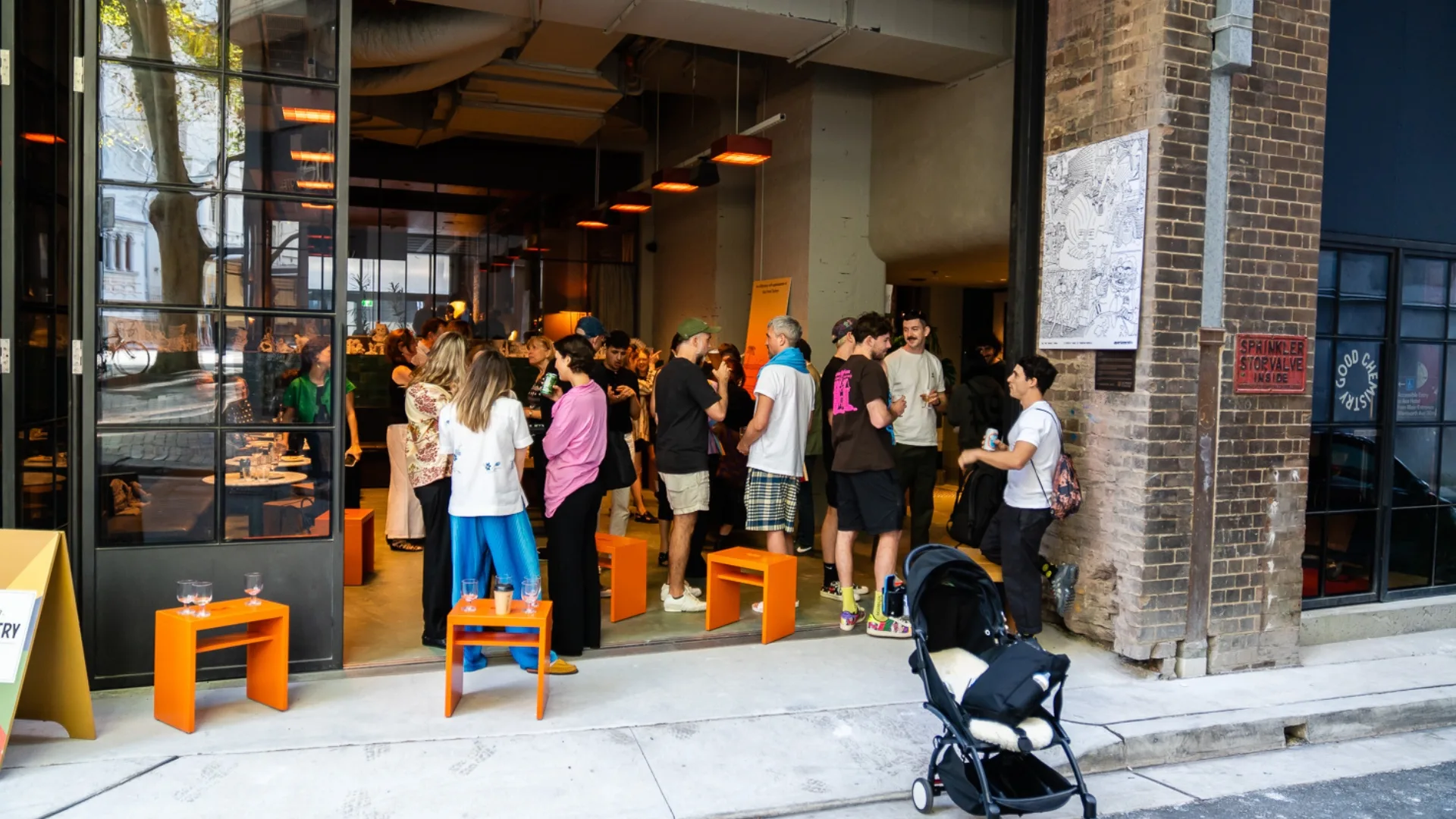A laneway in Sydney's Surry Hills buzzing with locals drinking beers and standing around orange stools