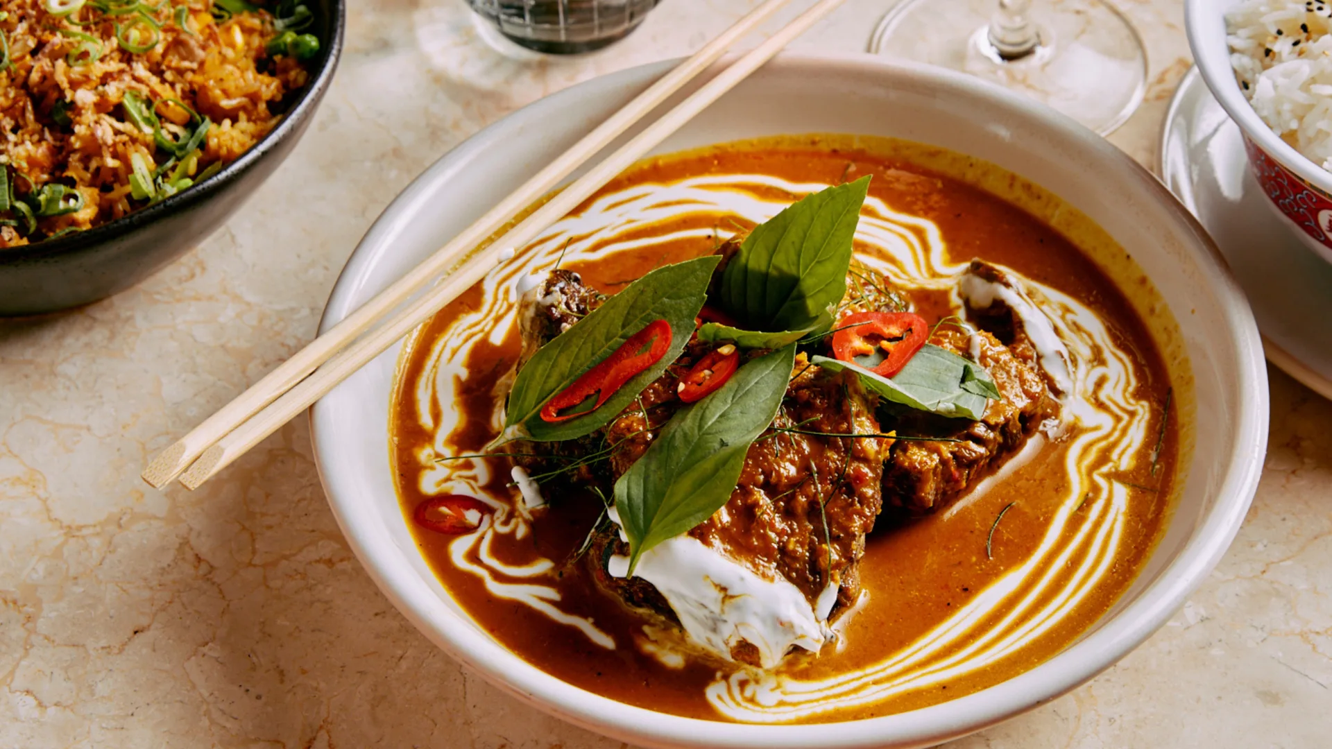 A vibrant bowl of beef rendang topped with chilli and coconut cream.