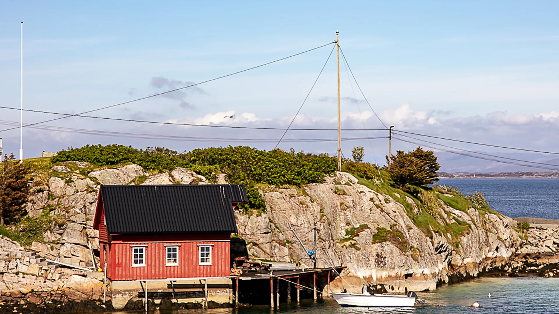 A red timber boathouse on the water's edge in Norway