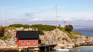 A red timber boathouse on the water's edge in Norway