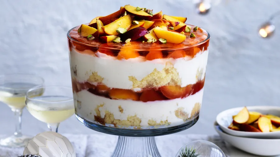 Picture of a clear glass bowl filled with layers of peach pavlova trifle with brandy custard