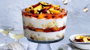 Picture of a clear glass bowl filled with layers of peach pavlova trifle with brandy custard