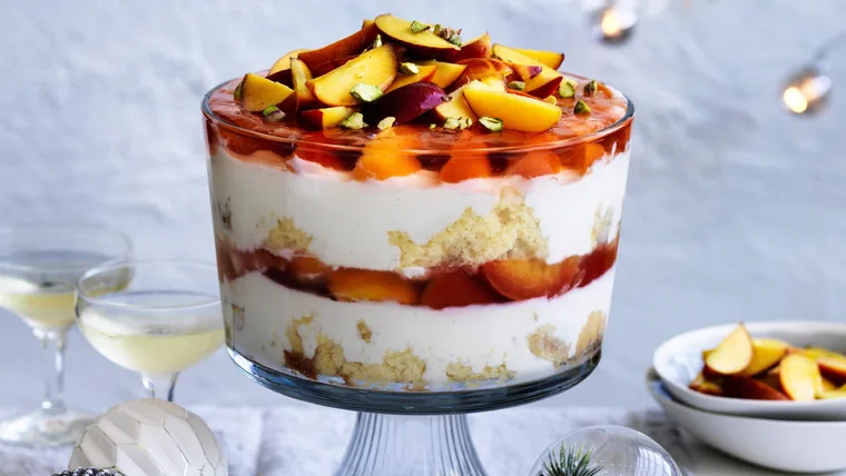 Picture of a clear glass bowl filled with layers of peach pavlova trifle with brandy custard