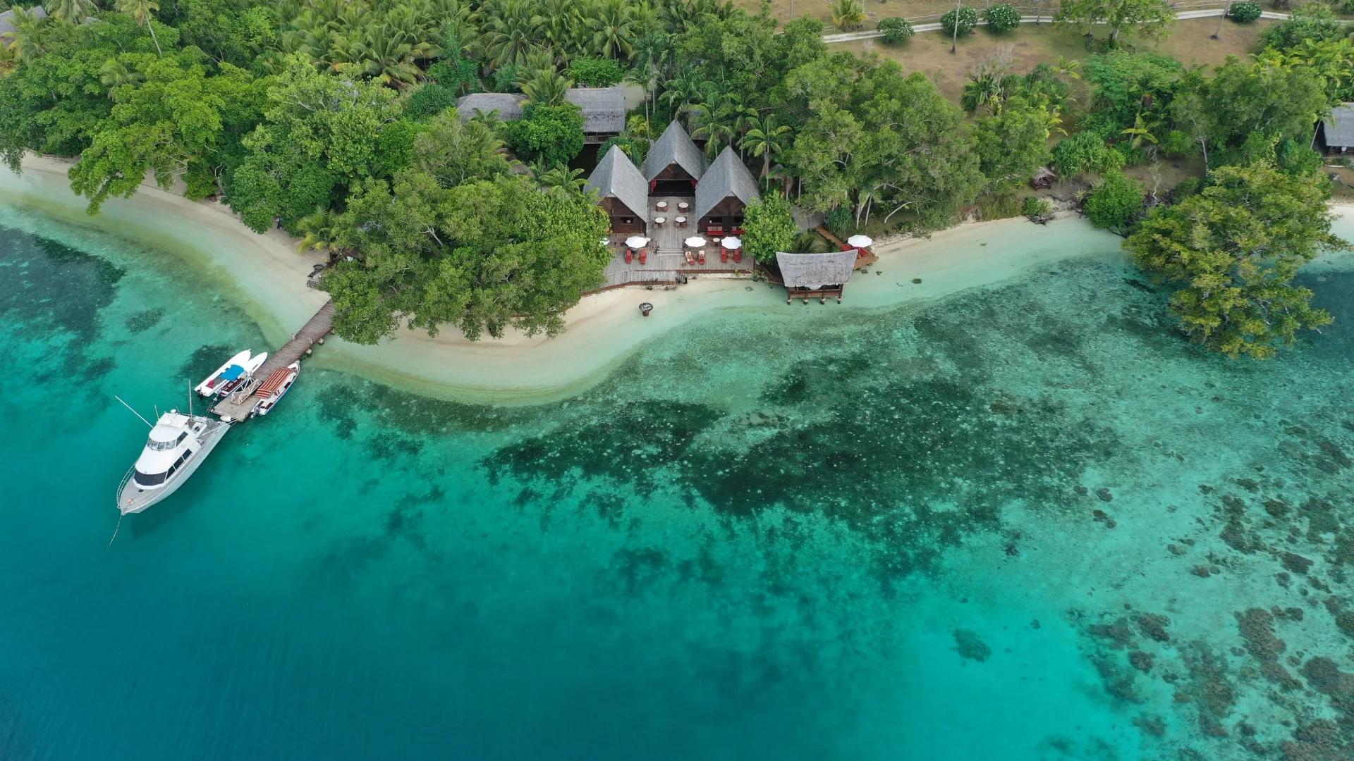 Aerial shot of blue waters wrapping around a clean shore surrounded by trees and greenery