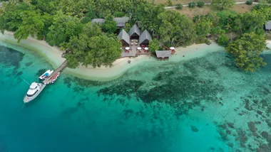 Aerial shot of blue waters wrapping around a clean shore surrounded by trees and greenery
