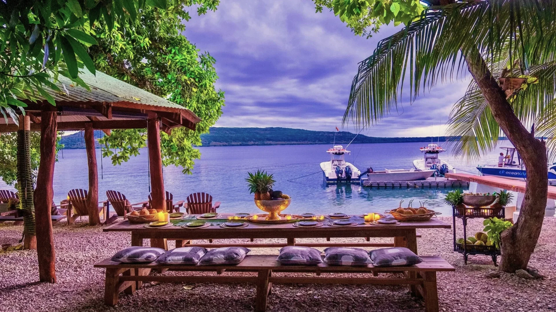 A photograph of a long dining table on shore between trees