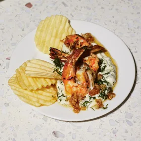 grilled prawns on a white dipping sauce with herbs with crinkle cut potato chips on the side