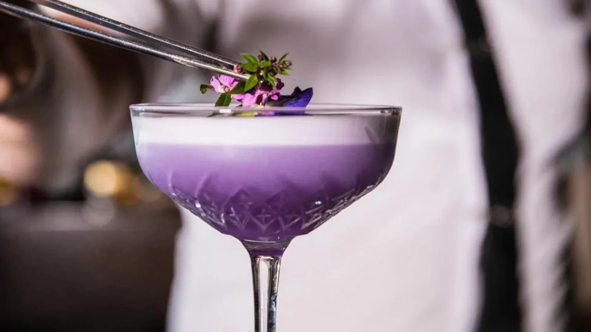 A purple cocktail with white foam, crowned with edible flowers 