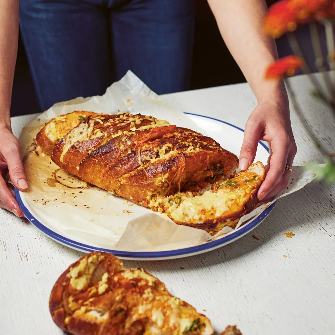 a woman tearing a piece of kimchi garlic bread off the loaf