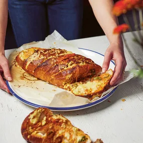 a woman tearing a piece of kimchi garlic bread off the loaf