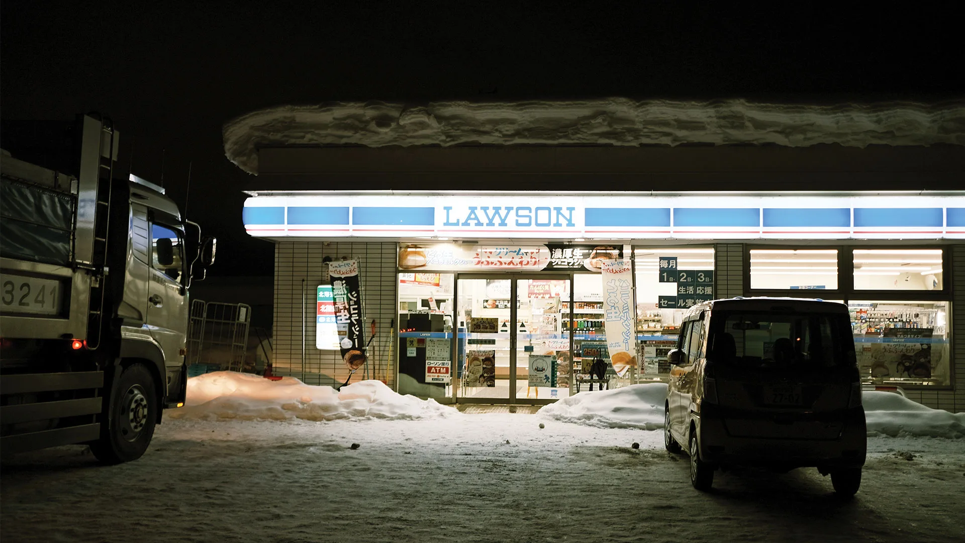 A low-lit picture of a Lawson convenient store with its roof covered in snow in Japan