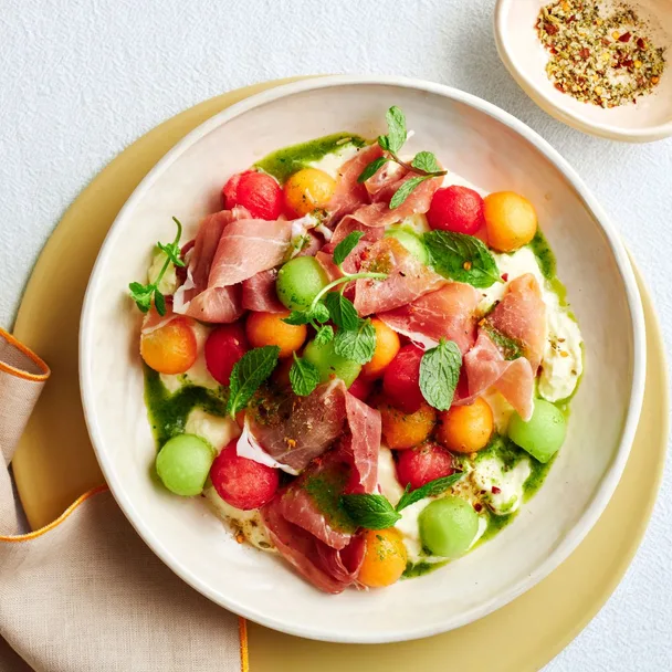melon balls with prosciutto and straciatella salad on a plate