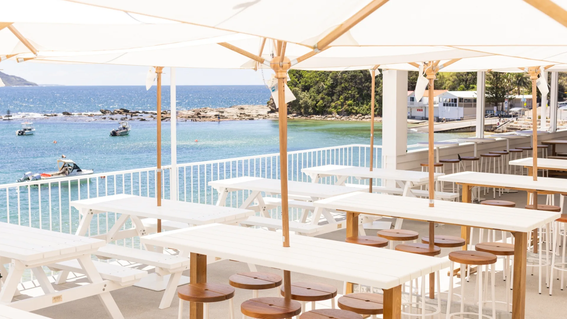 White wooden tables and timber stools on the deck looking out to the water at Terrigal Pavilion
