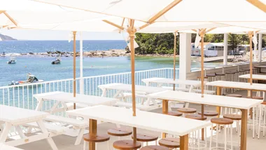 White wooden tables and timber stools on the deck looking out to the water at Terrigal Pavilion