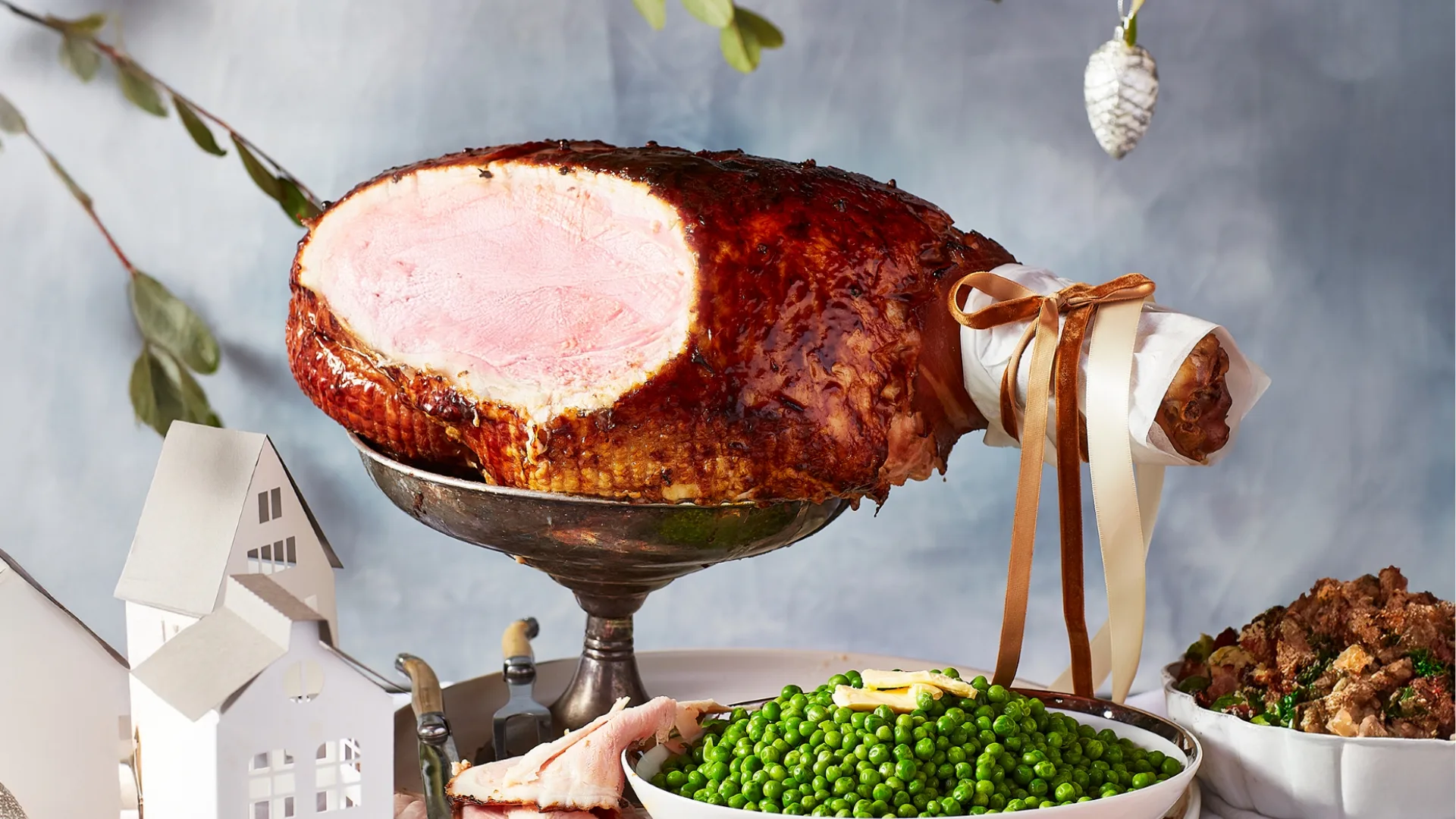 A Christmas ham that's been carved placed on a table with a side of peas and various Christmas side dishes
