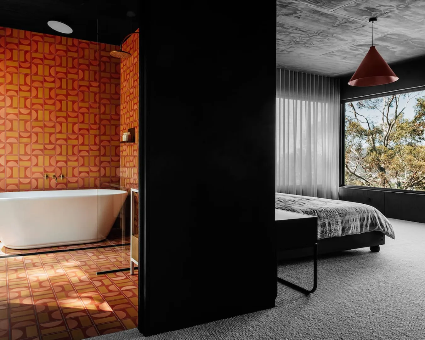 The orange bathroom with a bathtub and the main bedroom of Slow Beam, a Hobart Airbnb surrounded by bushland.